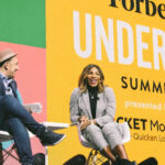 Two people seated on stage with a backdrop