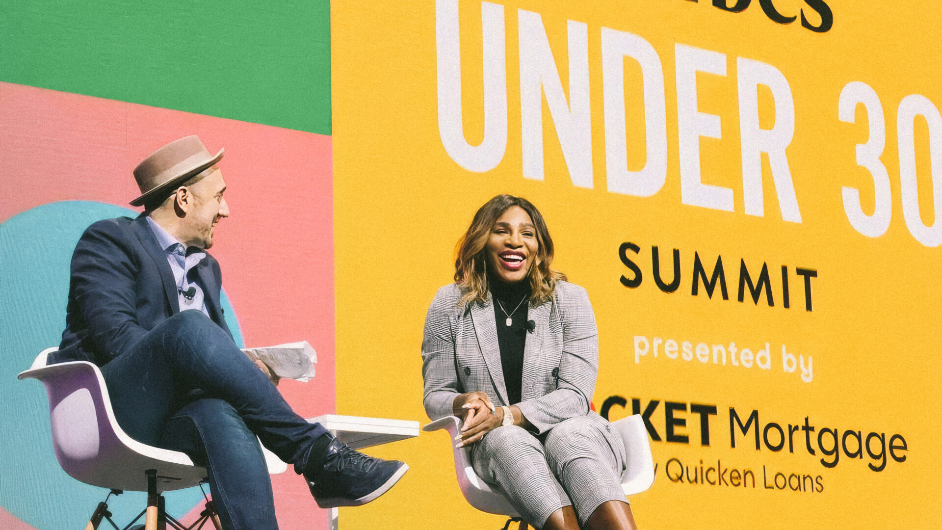 Two people seated on stage with a backdrop