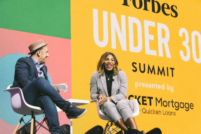 Two people seated on stage with a backdrop