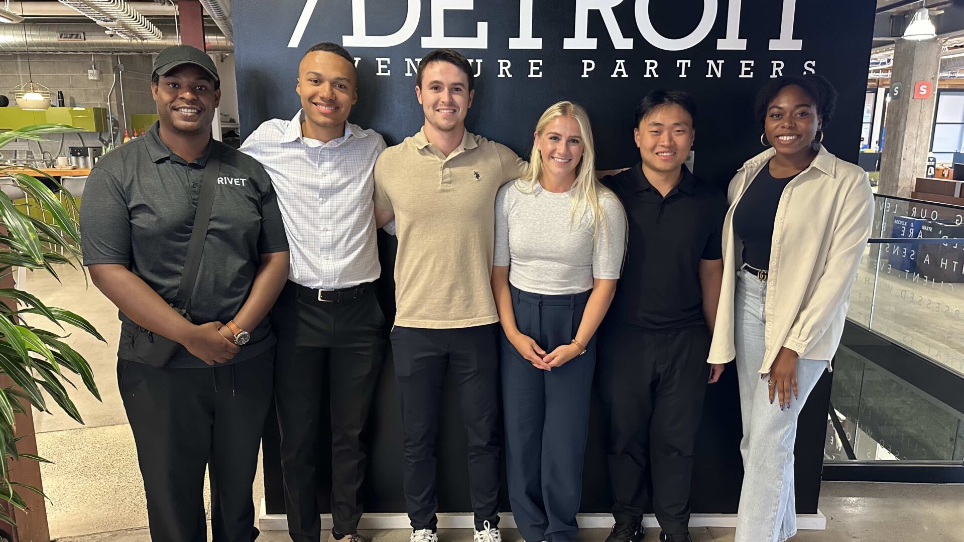 A photo of the 2024 Detroit Venture Partners fellows in front of a wall with Detroit Venture Partners on it