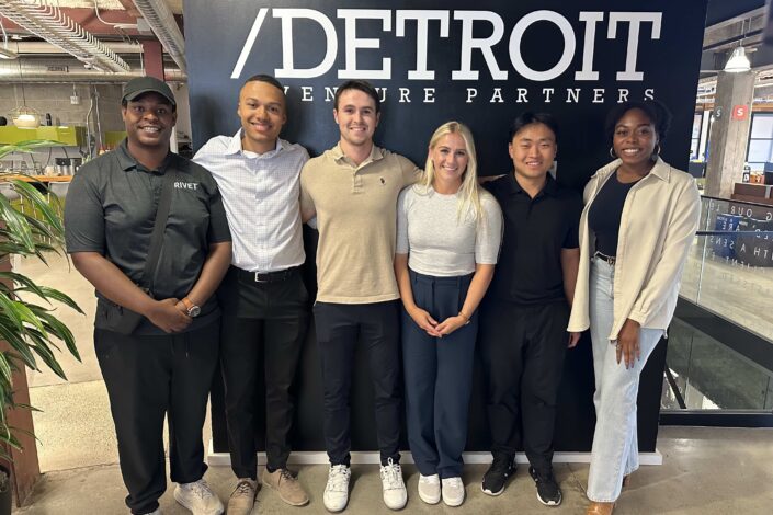 A photo of the 2024 Detroit Venture Partners fellows in front of a wall with Detroit Venture Partners on it