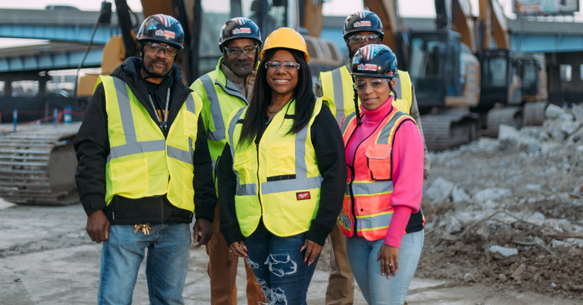 Picture of five people wearing yellow reflective vests at a construction site and wearing construction helmets