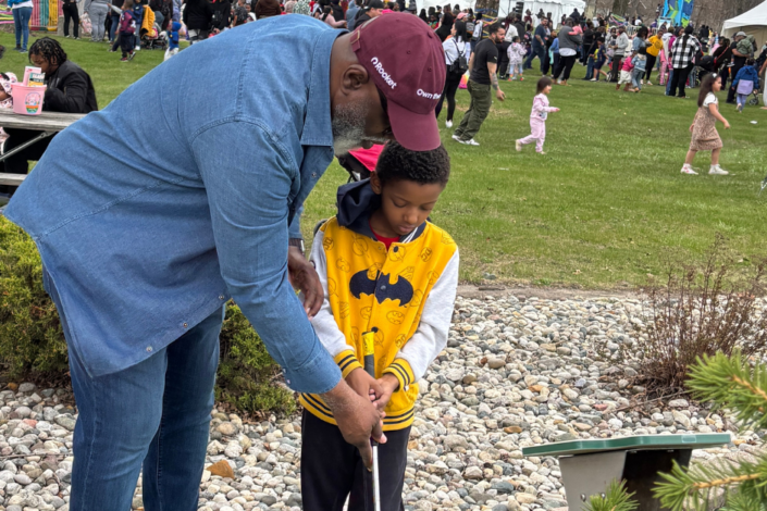 Picture of Eric helping a child by showing him how to putt a golf ball.