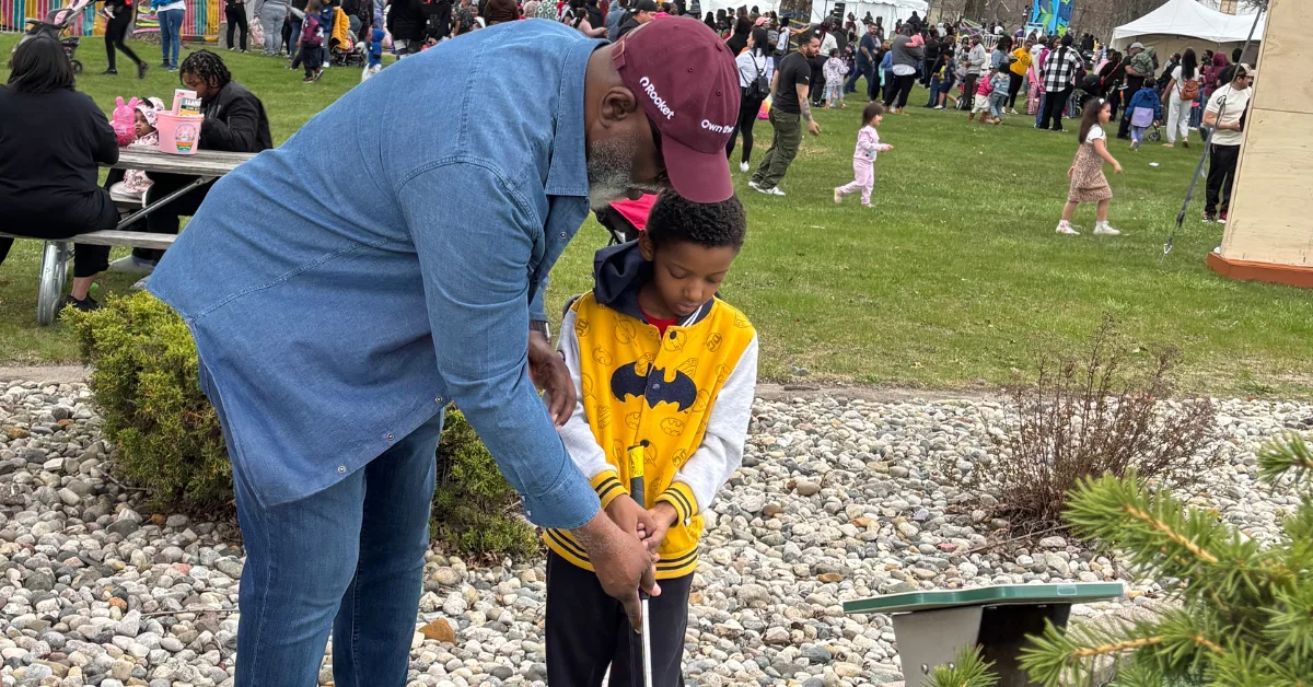 Picture of Eric helping a child by showing him how to putt a golf ball.